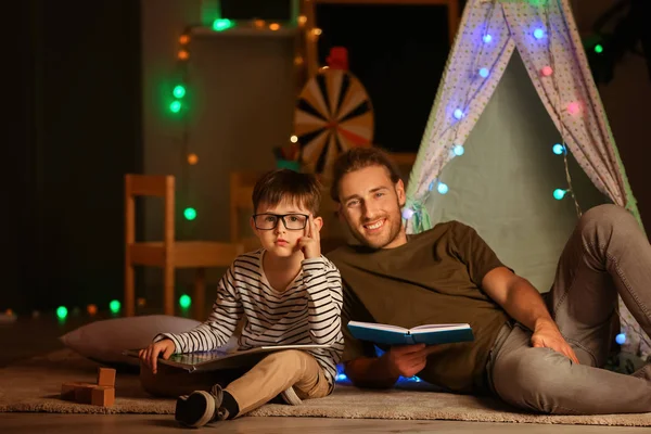 Far och hans son läser böcker hemma på kvällen. — Stockfoto