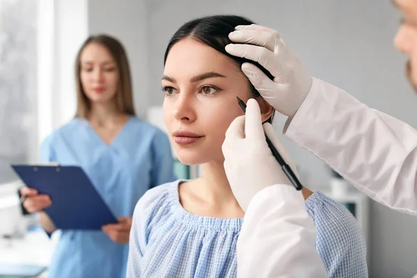 Plastic surgeon applying marks on patient's face in clinic — Stock Photo, Image