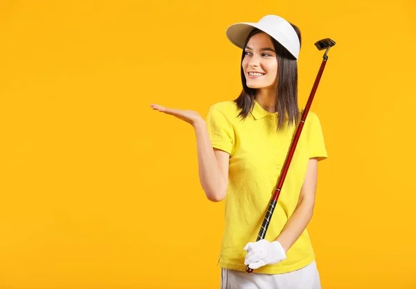 Beautiful female golfer showing something on color background — 스톡 사진