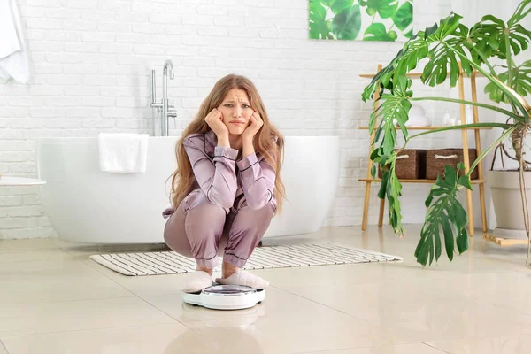 Droevige jonge vrouw op weegschaal in de badkamer. Dieetconcept — Stockfoto