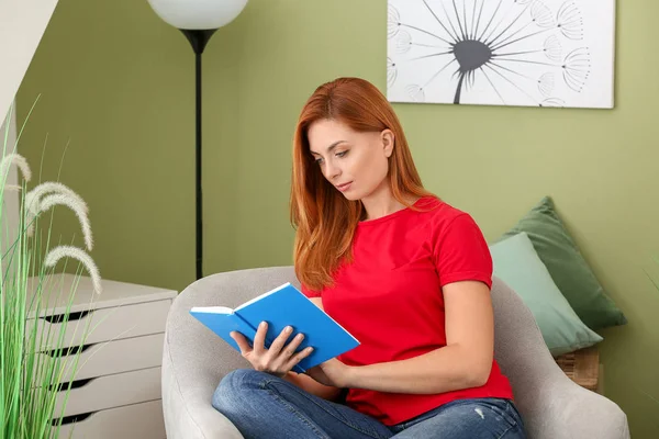 Beautiful woman reading book while sitting in armchair at home — Stock Photo, Image