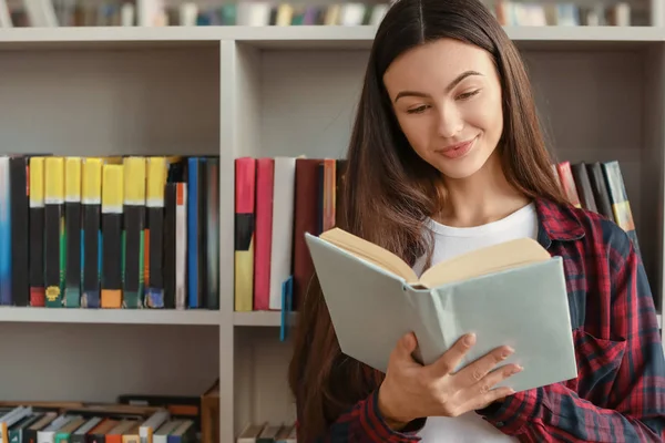 Estudiante leyendo libro mientras se prepara para el examen en la biblioteca —  Fotos de Stock