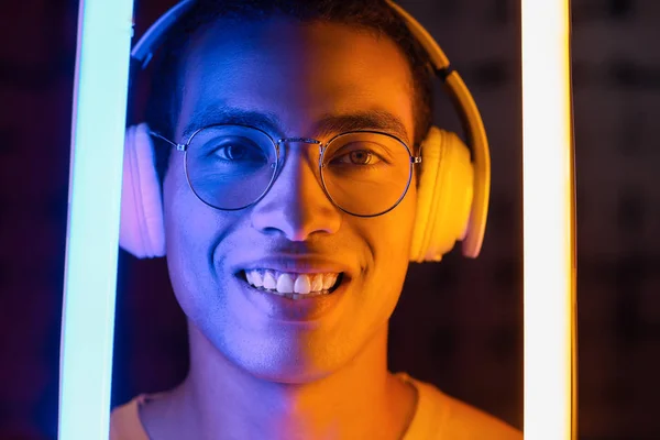 Toned portrait of African-American man with headphones and neon lamps on dark background — Stock Photo, Image