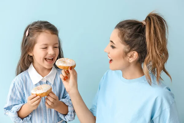 Beautiful young woman and little girl with donuts on color background — Stock Photo, Image