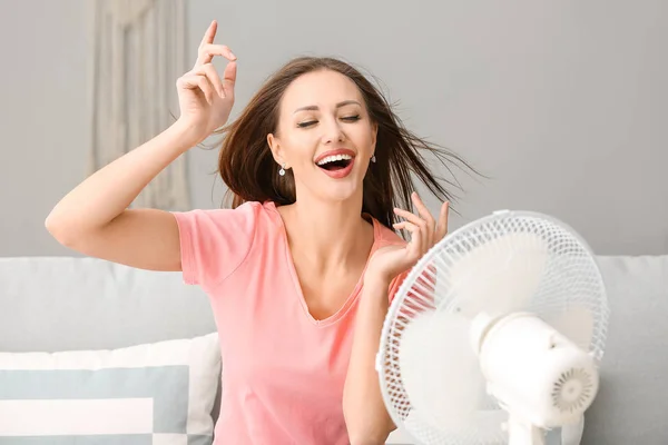 Mujer joven usando ventilador eléctrico durante la ola de calor en casa —  Fotos de Stock