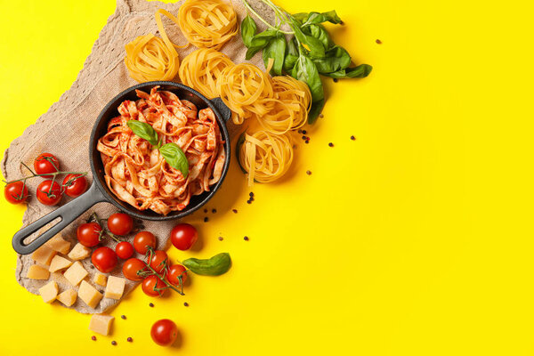 Сковородка с вареной, сырой пастой и томатным соусом на цветном фоне
