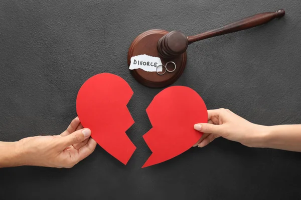 Hands of couple with broken heart and judge\'s gavel on dark background. Concept of divorce