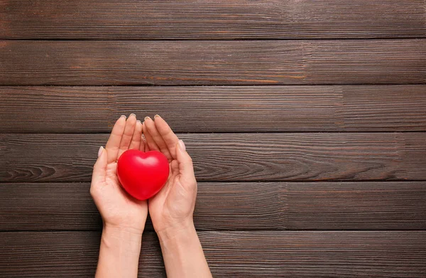 Mãos femininas com coração no fundo de madeira. Conceito de cardiologia — Fotografia de Stock