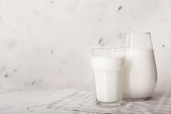 Bicchiere e brocca di latte saporito su sfondo bianco — Foto Stock