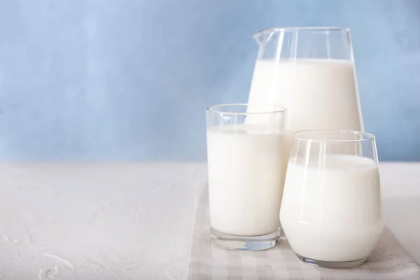 Glasses and jug of tasty milk on white table — 스톡 사진