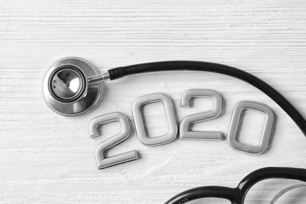 Stethoscope and figure 2020 on white wooden background