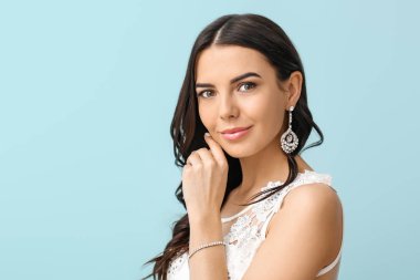 Young bride with beautiful jewelry on color background