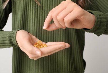 Young woman with fish oil on light background, closeup