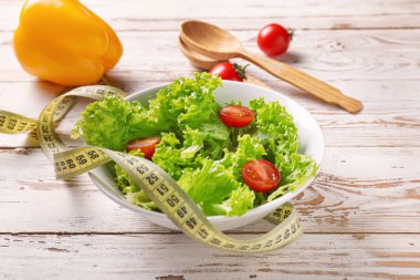 Healthy salad with measuring tape on wooden background. Diet concept