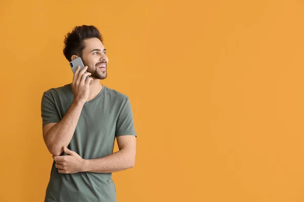 Happy young man talking by mobile phone on color background — Stock Photo, Image