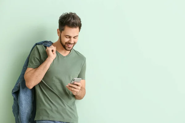 Щасливий молодий чоловік з мобільним телефоном на кольоровому фоні — стокове фото
