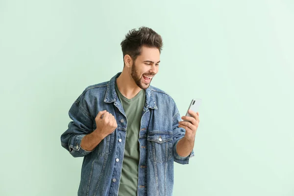 Щасливий молодий чоловік з мобільним телефоном на кольоровому фоні — стокове фото