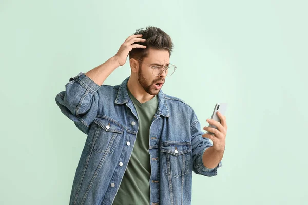 Shocked young man with mobile phone on color background — Stock Photo, Image