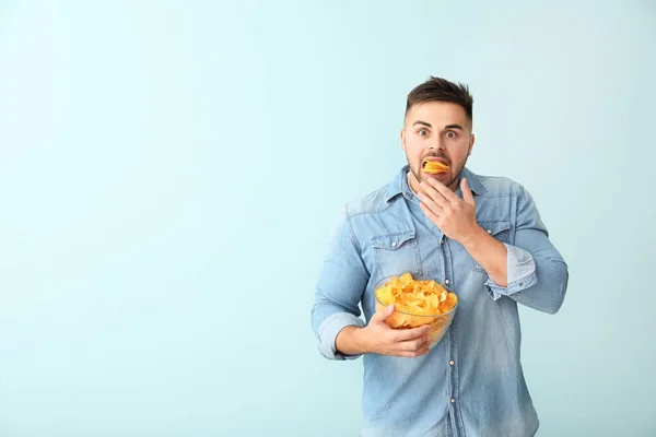 Shocked young man with tasty potato chips on color background — Stock Photo, Image