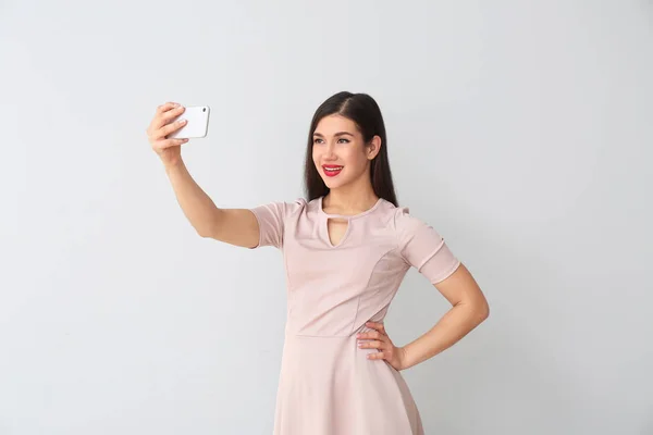 Beautiful young woman taking selfie on light background — Stock Photo, Image