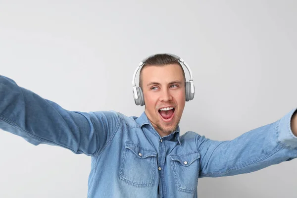 Handsome young man with headphones taking selfie on light background — Stock Photo, Image