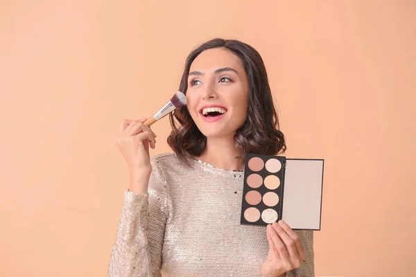 Beautiful young woman applying makeup on color background — Stock Photo, Image