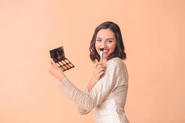 Beautiful young woman applying makeup on color background — Stock Photo, Image
