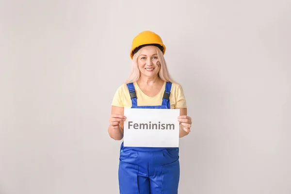 女性の労働者は、光の背景に単語フェミニズムと紙を保持 — ストック写真