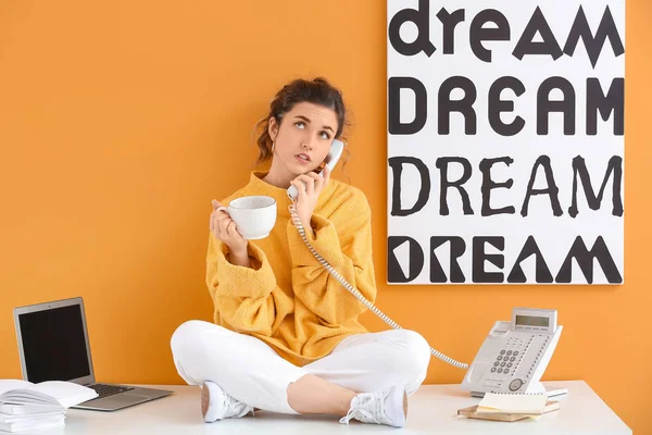 Beautiful young woman with cup of tea talking by phone against color background — 스톡 사진