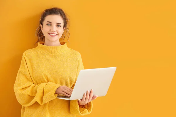 Красивая молодая женщина в теплом свитере и с ноутбуком на цветном фоне — стоковое фото