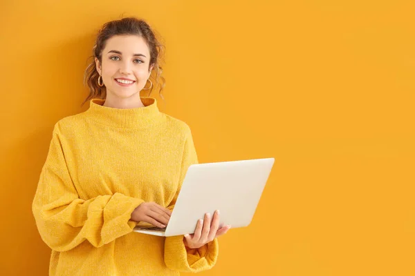 Beautiful young woman in warm sweater and with laptop on color background — 스톡 사진