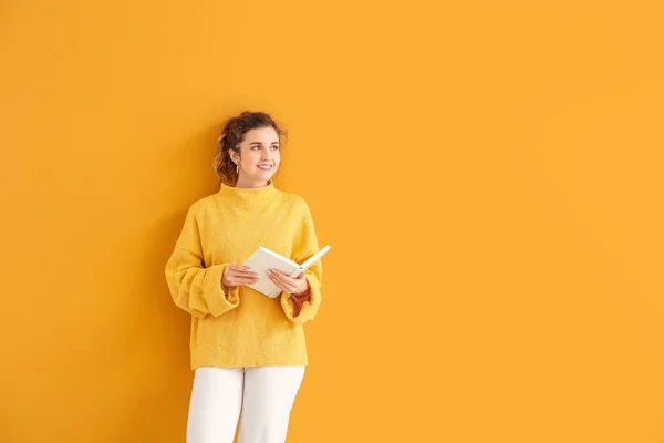 Beautiful young woman in warm sweater and with book on color background — 스톡 사진