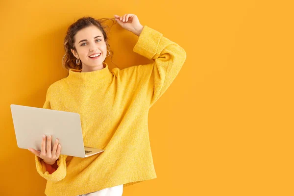 Hermosa mujer joven en suéter cálido y con ordenador portátil en el fondo de color — Foto de Stock