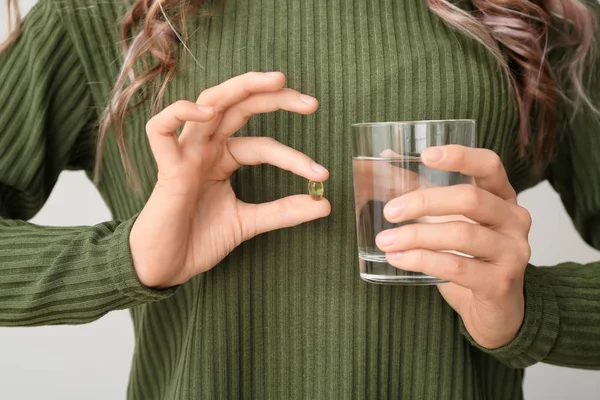 Young woman with fish oil on light background, closeup — Stok fotoğraf