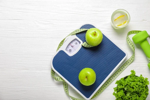 Different healthy food with measuring tape, scales and dumbbells on white wooden background. Diet concept — Stok fotoğraf