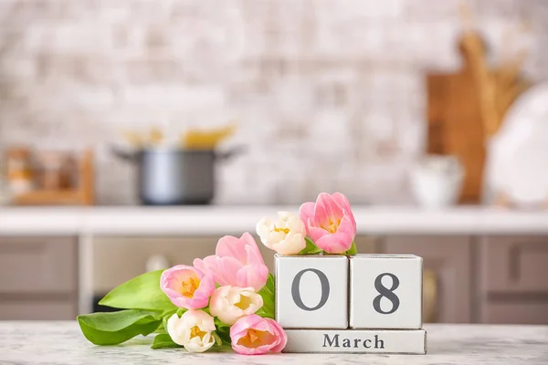 Calendar with date of International Women's Day and flowers on table in kitchen — Stock Photo, Image