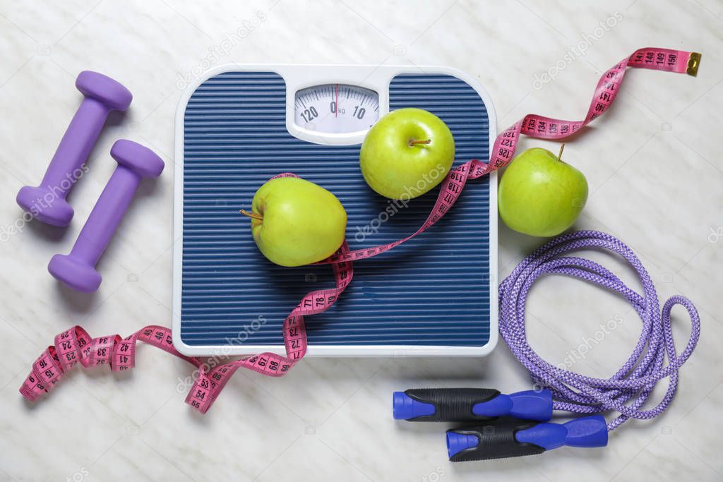 Apples, scales, dumbbells, jumping rope and measuring tape on light background. Diet concept