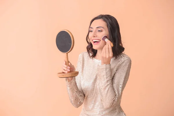 Krásná mladá žena použití make-up na barevném pozadí — Stock fotografie