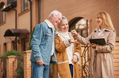 Emlakçı evin anahtarını açık havada yaşlı bir çifte veriyor.