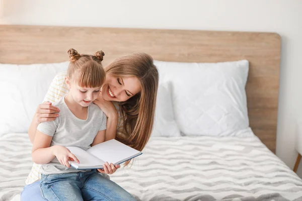 Vacker ung kvinna och hennes lilla dotter läser bok hemma — Stockfoto