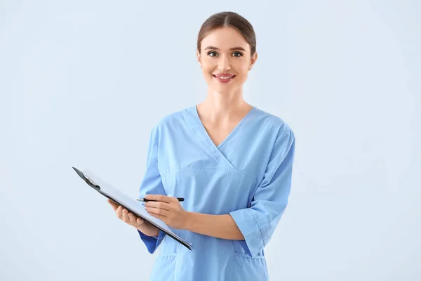 Portrait of female doctor with clipboard on light background — Stock Photo, Image