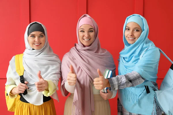 Muslimische Studentinnen zeigen Daumen nach oben auf farbigem Hintergrund — Stockfoto
