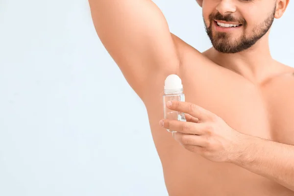 Handsome young man using deodorant on color background — Stock Photo, Image