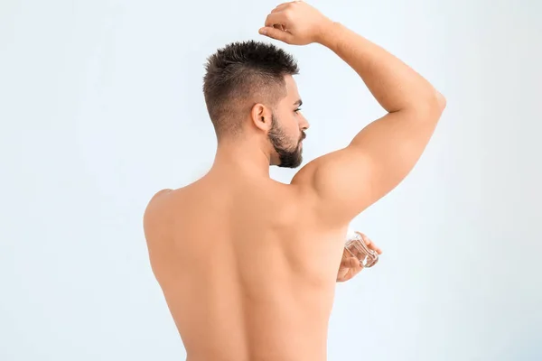 Handsome young man using deodorant on color background