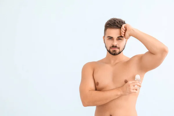 Bello giovane uomo utilizzando deodorante su sfondo di colore — Foto Stock