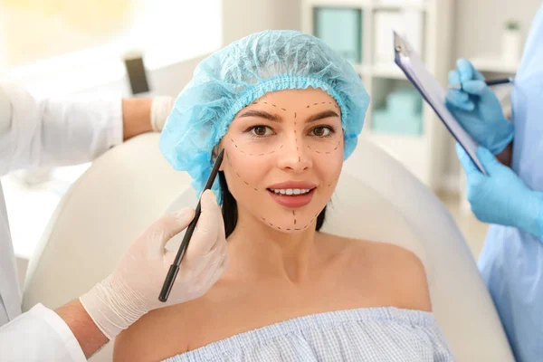 Plastic surgeon applying marks on patient's face in clinic — Stock Photo, Image