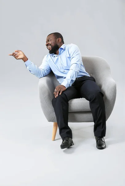 African-American man sitting in armchair against grey background — Stock Photo, Image