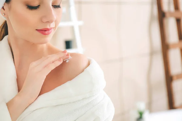 Beautiful young woman applying cream on her shoulder in bathroom — Stock Photo, Image