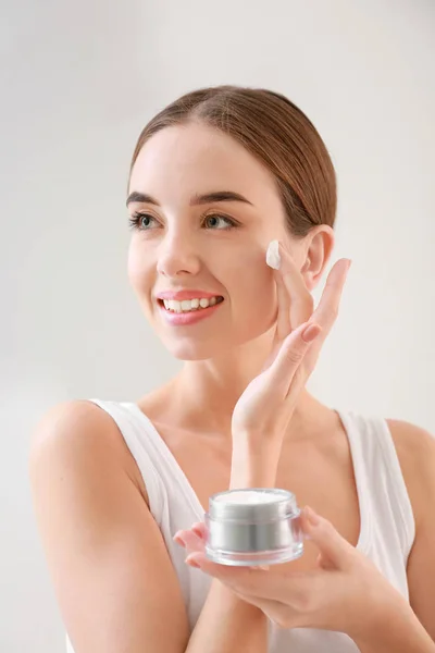 Hermosa joven con tarro de crema sobre fondo claro — Foto de Stock