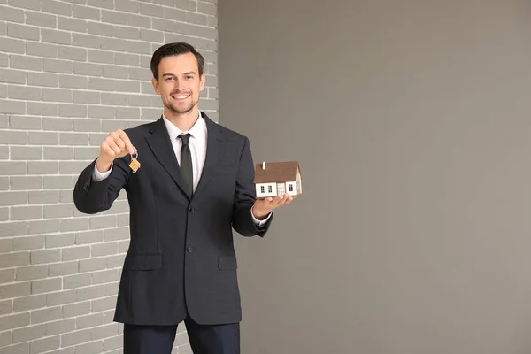 Retrato de agente imobiliário masculino com chave e modelo de casa dentro de casa — Fotografia de Stock